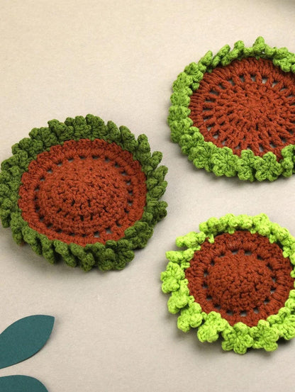 Three circular crochet coasters with brown centres and raised light and dark green flower edges.