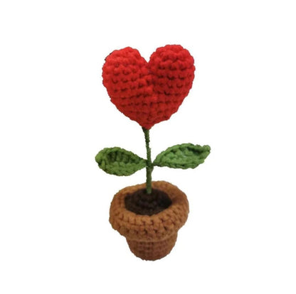 Red crocheted heart flower with green leaves in a brown handmade pot.