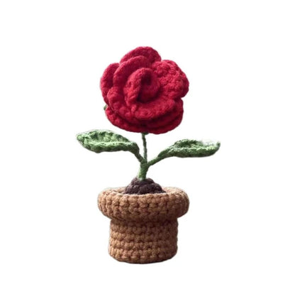 Red crocheted rose with green leaves and brown flowerpot on white background.
