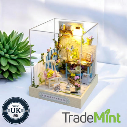 Corner of Garden miniature dollhouse craft scene with blue gate, tiny table, flowers and warm lamp inside a clear display case.