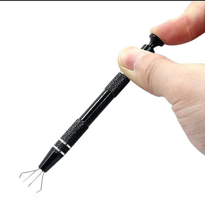 Close-up of a black four-prong pickup pen held between fingers with the flexible wire gripping claws extended.