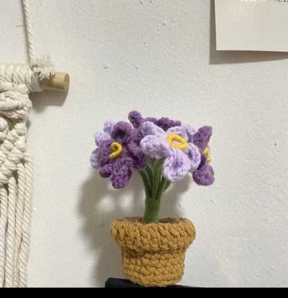 Purple crochet flower cluster with yellow centres in a small brown pot.
