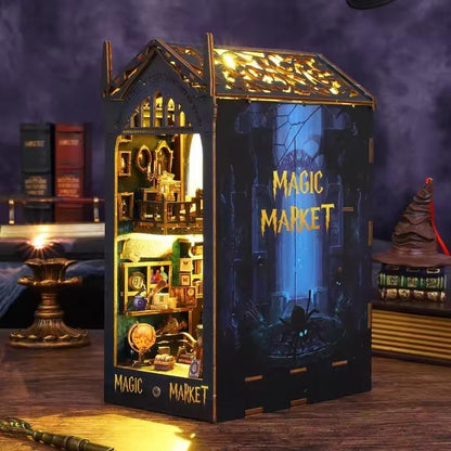Magic Market LED book nook displayed between books, with a golden illuminated miniature shop interior and dark blue side panel.