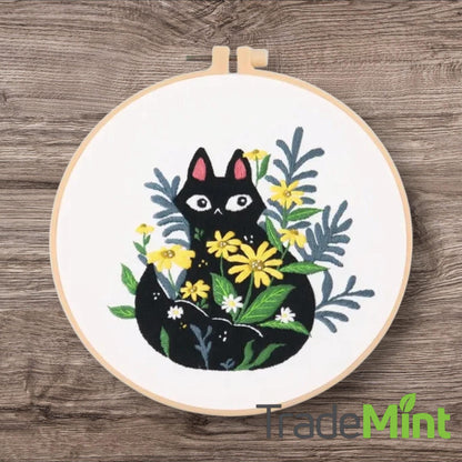 Black kitten with pink ears surrounded by yellow daisies and blue-green leaves embroidered in hoop.