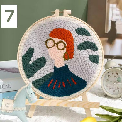 Punch needle embroidered portrait of a person with glasses and red hair among green leaves.