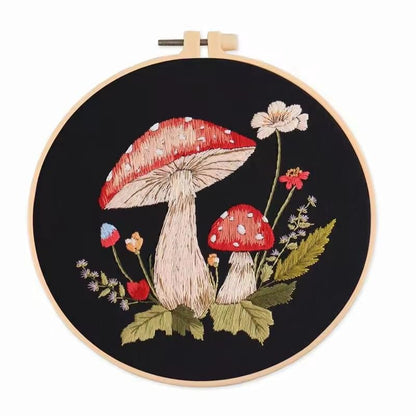 Two red and cream mushrooms stitched on black fabric with green leaves and pale wildflowers.