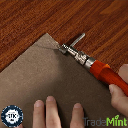 Hands using an adjustable leather edge groover along the corner of a brown leather sheet on a wooden table.
