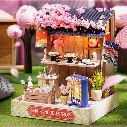 Sakura Noodles Shop miniature model with Japanese flags, ramen counter and pink blossom tree.