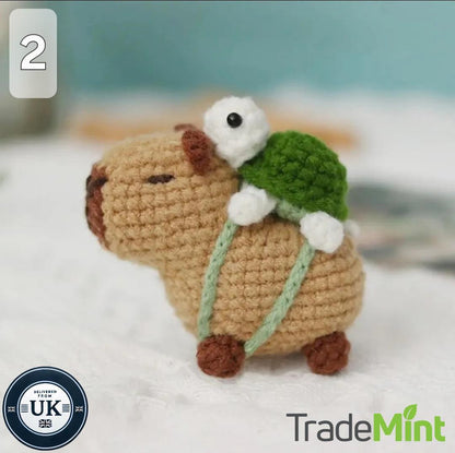 Side profile of a handmade crochet capybara with brown paws, green straps and a turtle on its back.