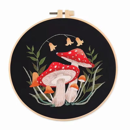 Mushroom embroidery design on black cloth with red toadstools, orange bells and tall green leaves.
