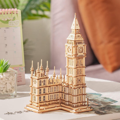 Wooden Big Ben clock tower model displayed on a table beside a desk calendar and small succulent plant.
