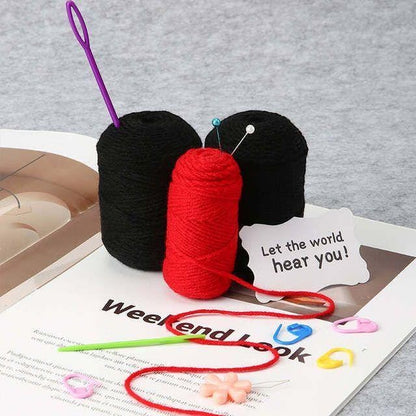 Black and red crochet yarn skeins with a purple needle and stitch markers for the Halloween dragon project.