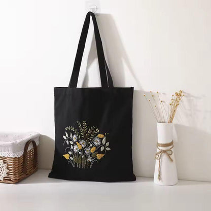 Black embroidery tote bag with colourful white and yellow wildflower bouquet hanging on wall.