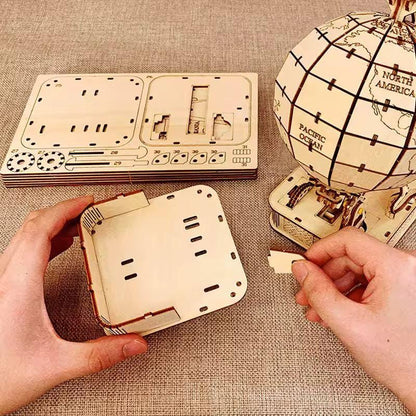 Hands assembling the wooden base of a globe puzzle with laser-cut components and partially completed globe nearby.