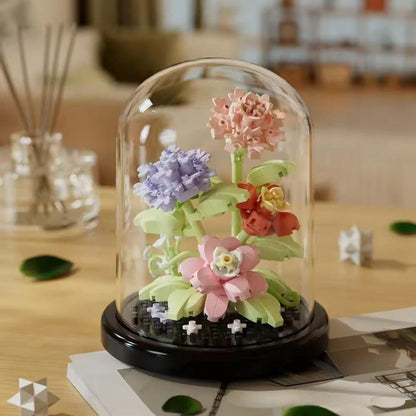 Pink, lilac and coral miniature building block flowers displayed in clear dome on black base.