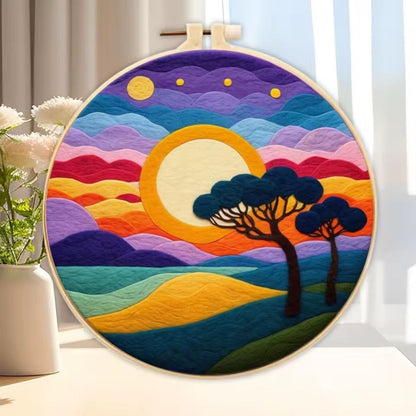Needle-felted colourful sunset artwork with yellow sun and silhouette trees inside wooden hoop.