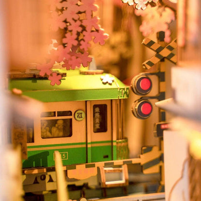 Close-up of miniature green Japanese tram and railway crossing signals under pink cherry blossoms.