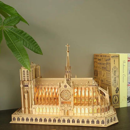Wooden Notre Dame cathedral model with warm LED lighting displayed on a shelf beside books and a houseplant.