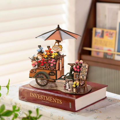 Rolife Blossom Cart 3D wooden puzzle with floral cart, bicycle and sunshade displayed on books.