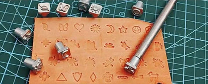 Leather surface stamped with 32 small decorative symbols beside metal punches and silver holder.