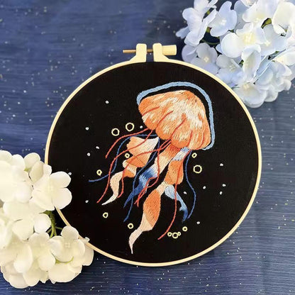 Orange jellyfish and fine blue tentacles embroidered on black fabric with decorative bubbles.