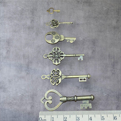 Six vintage bronze key pendants in different shapes shown alongside a centimetre ruler for scale.