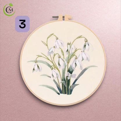 Floral embroidery design three depicting white snowdrop flowers with green leaves on cream fabric.