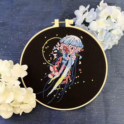 Blue jellyfish with pink floral tentacles and gold ring detail embroidered in a bamboo hoop.