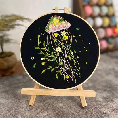 Jellyfish embroidered in green, lilac and yellow with trailing floral tentacles on black fabric.