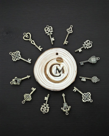 Twelve small ornate bronze key charms arranged around a circular engraved wooden Craft Mint disc.