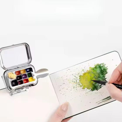 Hand painting green foliage with small travel watercolour set and brush on white sketchbook.