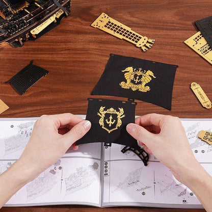 Hands preparing black sail pieces with gold emblems for Seahorse Barque ship model assembly.