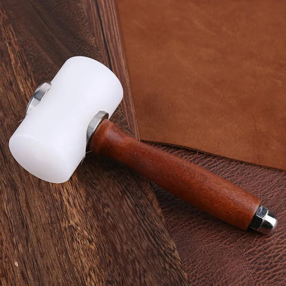 White nylon leathercraft mallet laid across brown leather pieces on a wooden surface.