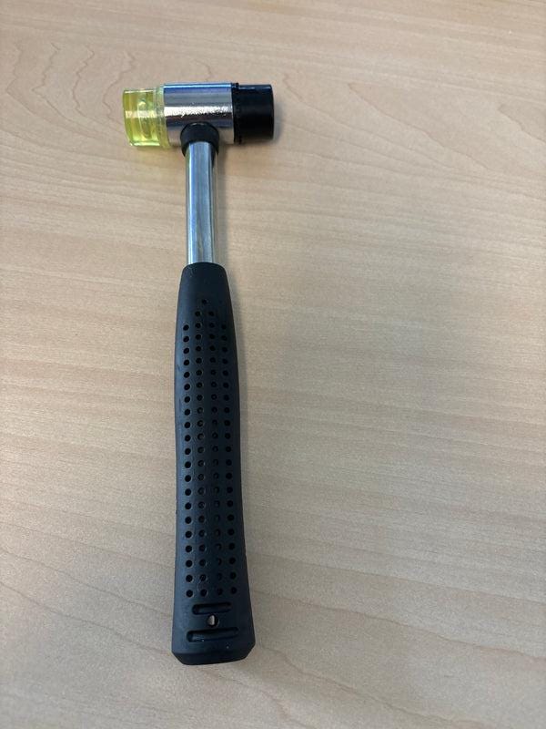 Silver-shaft leather craft hammer with black grip and two striking faces laid on a light wooden table.